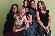Group of smiling women and girls posing together indoors against neutral background.