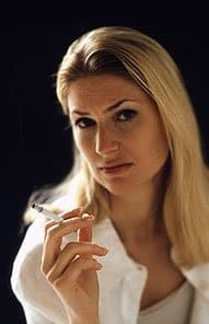 Professional woman in white coat holding tooth model against dark background for dental practice.