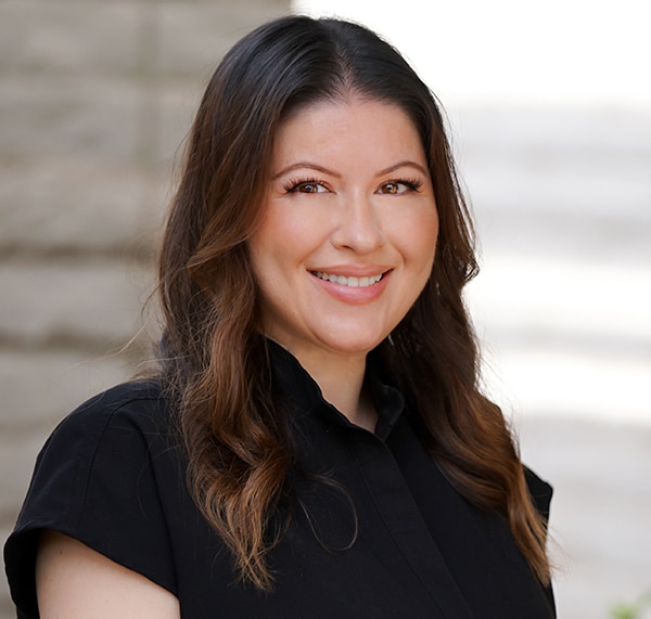 Professional headshot of a woman smiling at camera, wearing black shirt, neutral background.