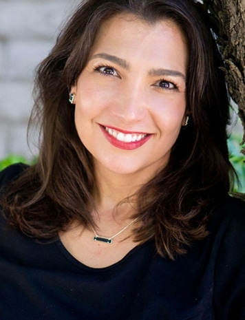 Professional headshot of smiling woman with dark hair against blurred background for dental practice.