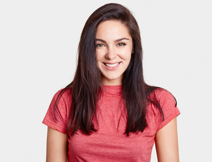Professional headshot of smiling woman with long dark hair wearing pink shirt against white background.