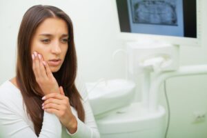 Woman with toothache holding her cheek while visiting a dental clinic for emergency care