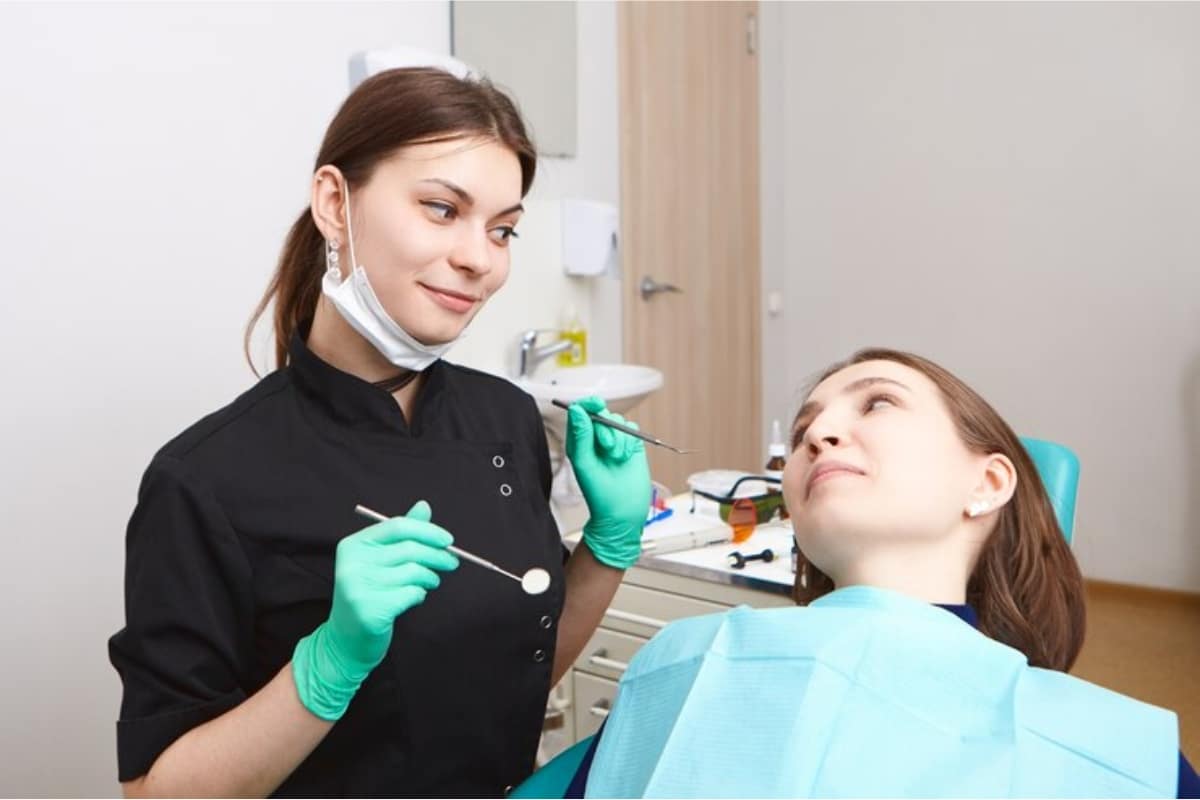 A cosmetic dentist in Tempe holding dental tools while checking teeth of female patient