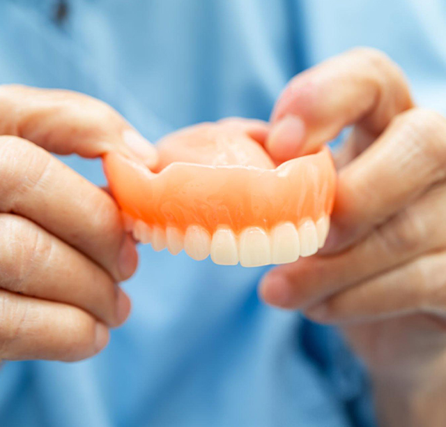 Dentist holding orange dentures against blue scrubs for demonstration purposes.