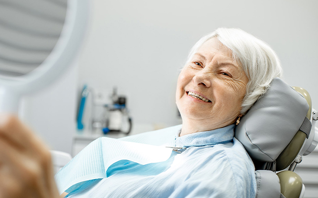 Senior woman smiling in dental chair during checkup at Okun Dentistry office.