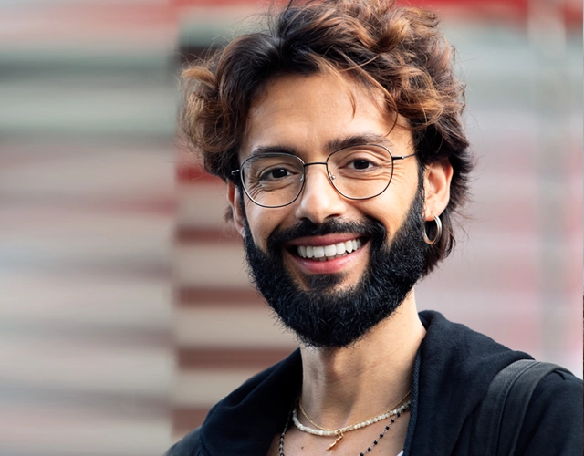 Smiling man with beard and glasses wearing black shirt against brick wall background.