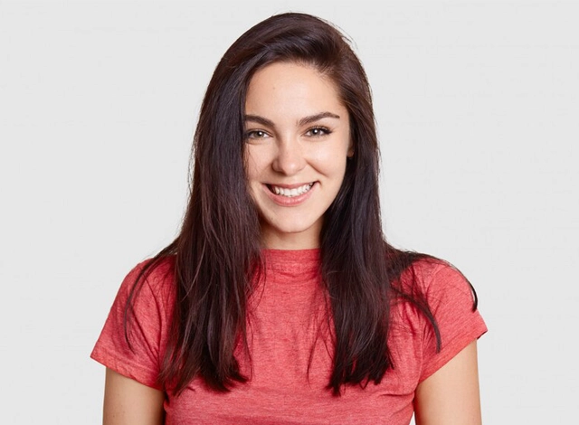 Smiling woman with long dark hair wearing red shirt against neutral background.
