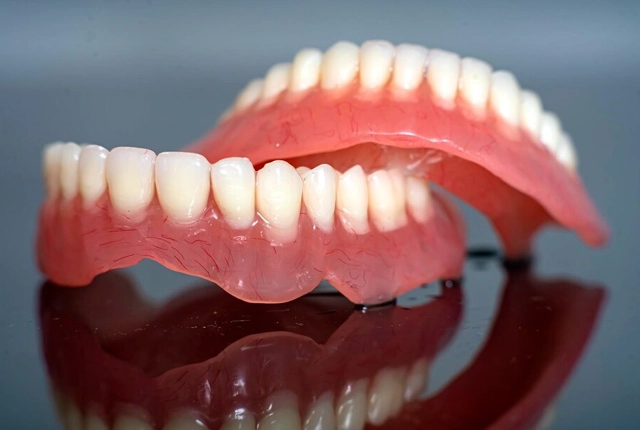 Pair of upper and lower dentures displayed on reflective surface showing artificial teeth alignment.