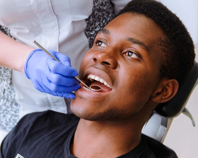 Dentist in blue gloves examining patient's teeth during dental checkup in clinical setting.