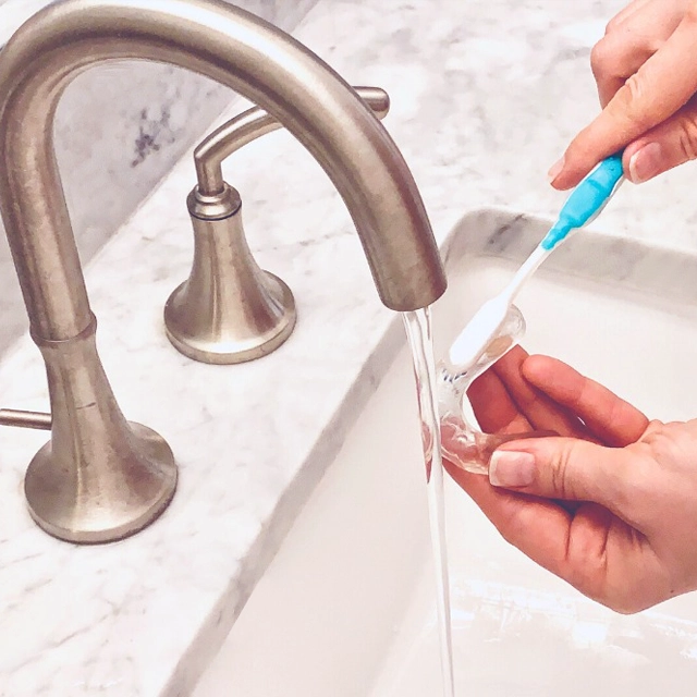 Person cleaning dental floss near sink with modern faucet and marble countertop.