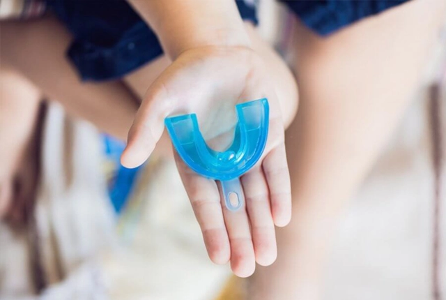 Child's hand holding blue mouthguard or dental retainer against blurred background.