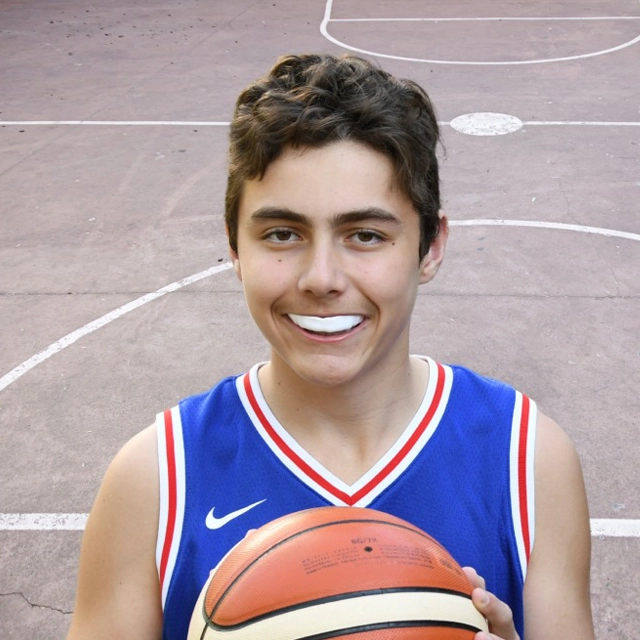 Young male basketball player in blue jersey holding ball on outdoor court.