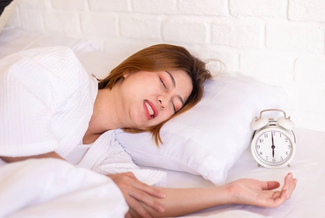 Woman sleeping peacefully in bed holding alarm clock showing early morning time.