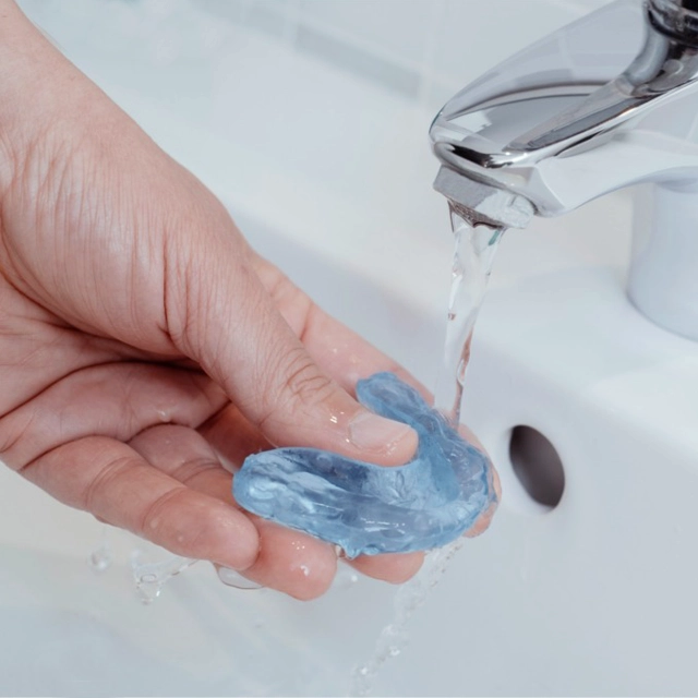 Person washing hands with blue soap under running water at sink.