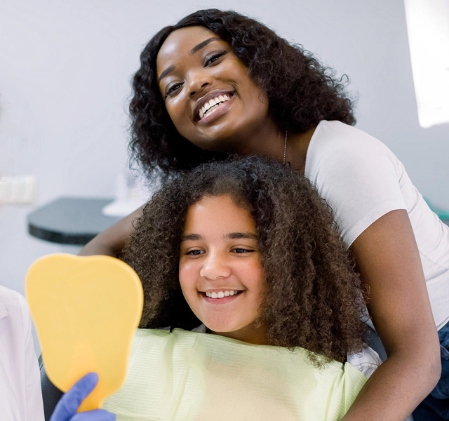 Woman and child smiling together in dental office setting, promoting family dental care.