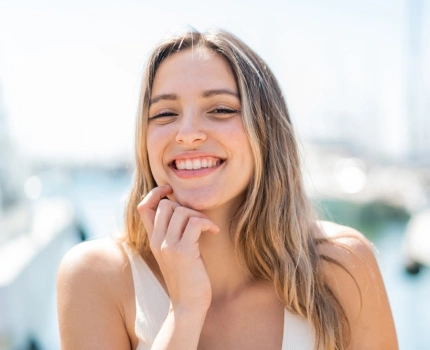 Smiling woman with hand near face in bright, urban rooftop setting for dental practice.