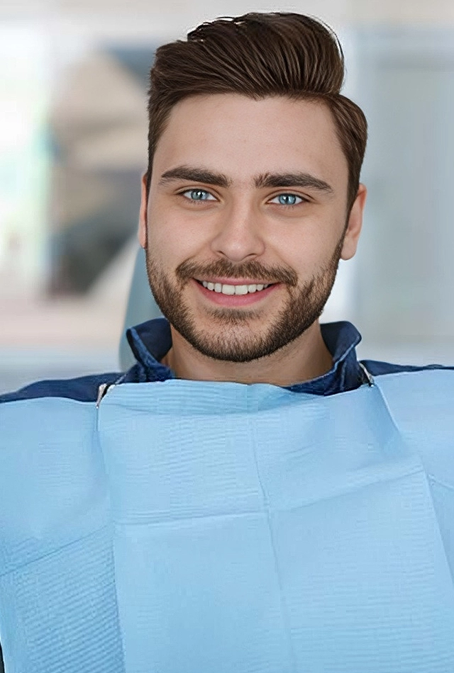 Young man smiling at camera wearing blue bib in dental office setting.