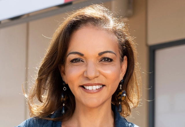 Professional portrait of smiling woman in dental office setting with neutral background.