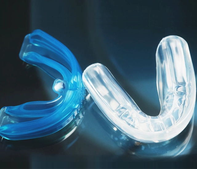 Clear and blue custom dental night guards on dark background for teeth protection.