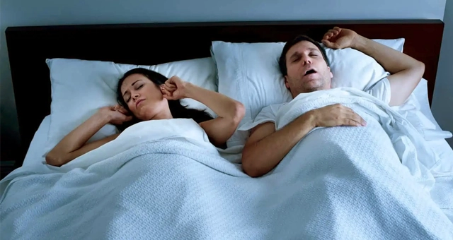 Two people lying in bed appearing uncomfortable or experiencing sleep issues, suggesting dental-related sleep problems.