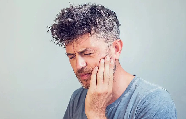 Man touching jaw in pain against neutral background, suggesting dental discomfort or toothache