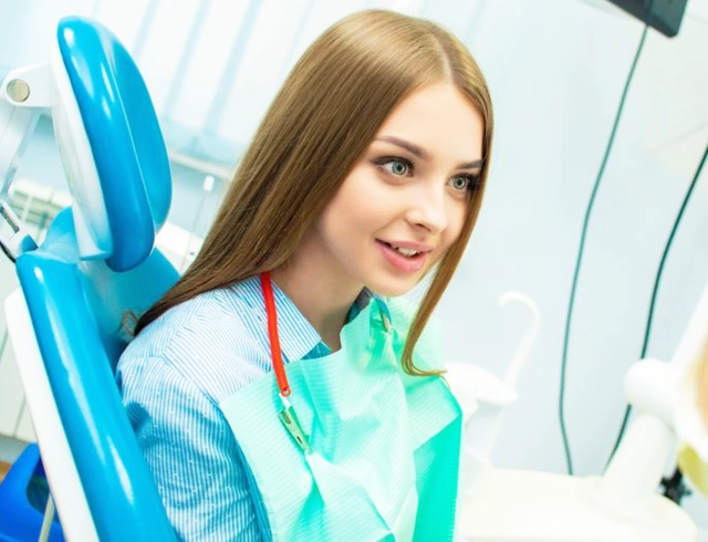 Female dentist in clinical attire smiling at dental office with equipment visible