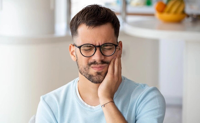 Man wearing glasses and light blue shirt smiling in dental office setting