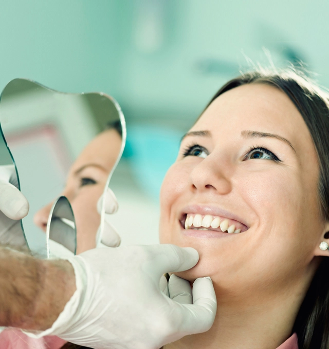 Smiling woman receiving dental examination from dentist wearing gloves and mirror in clinical setting.