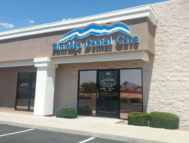 Okun Dentistry storefront with blue signage, entrance doors, and landscaping in strip mall setting.