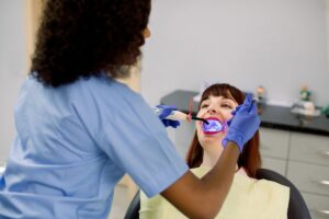 Dental professional examining patient's teeth in clinical setting with blue protective equipment.