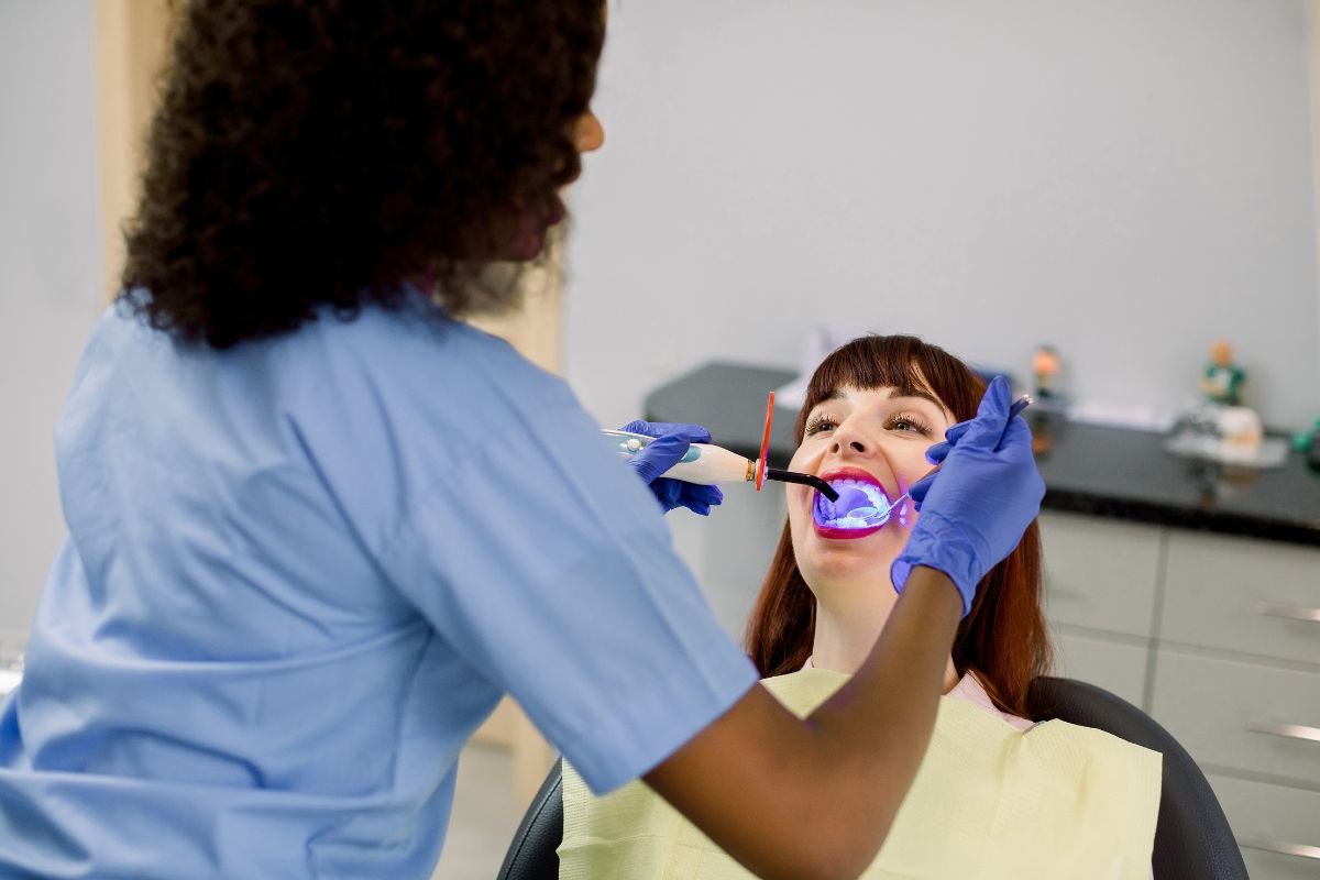 Dental professional examining patient's teeth in clinical setting with blue protective equipment.