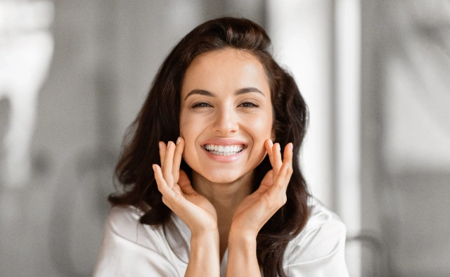 Smiling woman with hands to face in bright dental office setting, representing professional dental care.